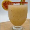 Vaso con bebida congelada frutal con borde de chile y rodajas de fruta como decoración.